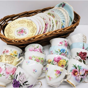 May include: A collection of vintage teacups and saucers with floral patterns in various colors, including pink, yellow, blue, and red. The cups and saucers are arranged in a wicker basket and on a table.