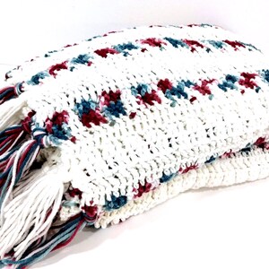 May include: White crocheted throw blanket with a fringe border. The blanket has a pattern of small red and blue flowers.