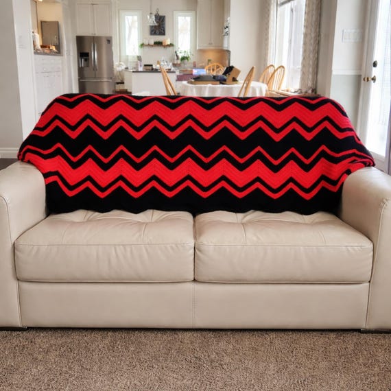 A chunky hand-crocheted chevron throw in bold cherry red and black — the kind of statement blanket that becomes the focal point of a room.