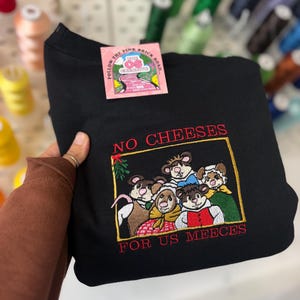 May include: Black sweatshirt with an embroidered design featuring cartoon mice and the text "NO CHEESES FOR US MEEECES" in red. A pink tag with text is attached to the sweatshirt.
