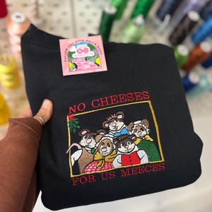 May include: Black sweatshirt with an embroidered design featuring a group of mice and the text "NO CHEESES FOR US MEEECES". The sweatshirt has a tag that reads "FOLLOW THE PINK BRICK ROAD".