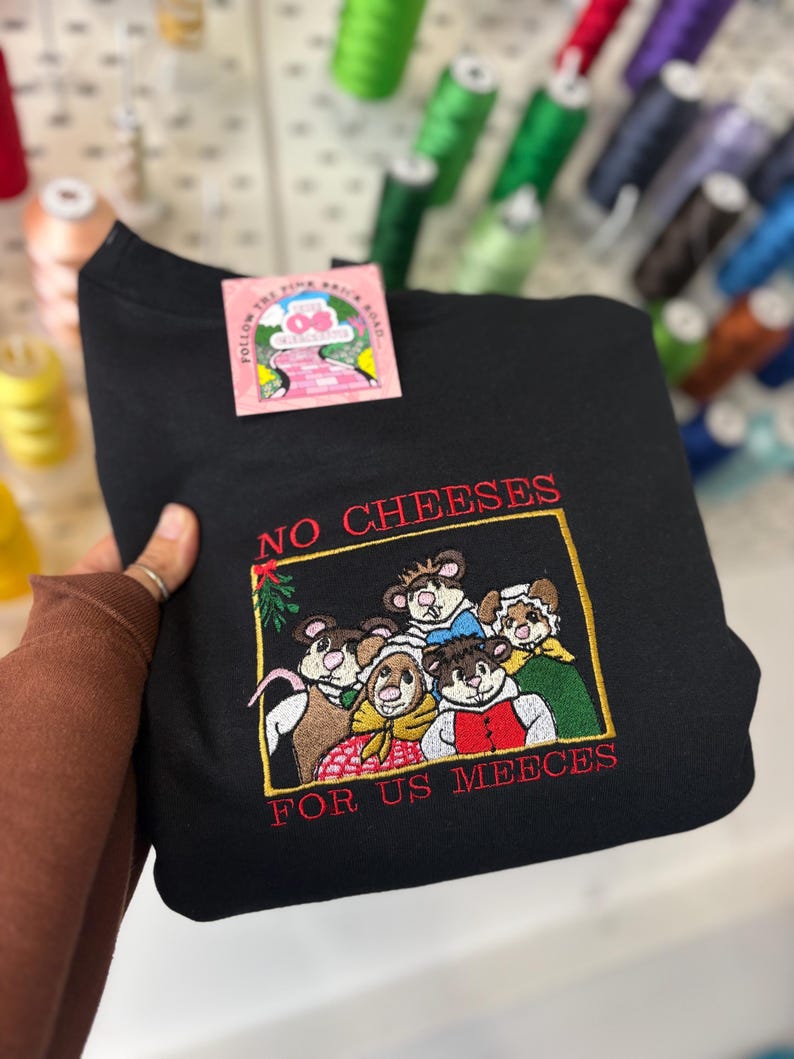 May include: Black sweatshirt with an embroidered design featuring a group of mice and the text "NO CHEESES FOR US MEEECES". The sweatshirt has a tag that reads "FOLLOW THE PINK BRICK ROAD".