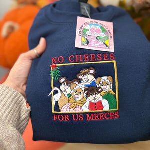 May include: Navy blue sweatshirt with an embroidered design featuring cartoon mice and the text "NO CHEESES FOR US MEECEES." The sweatshirt has a crew neck and a tag that reads "FOLLOW THE PINK BRICK ROAD... THE OS CREATIVE."