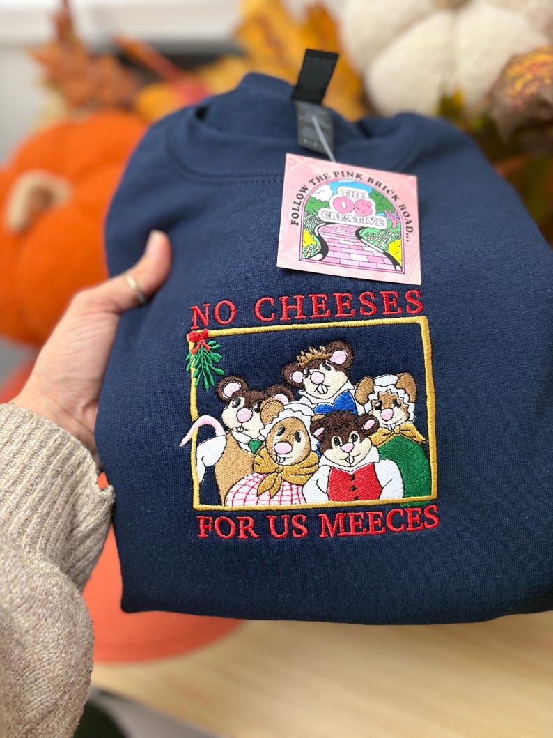 May include: Navy blue sweatshirt with an embroidered design featuring cartoon mice and the text "NO CHEESES FOR US MEECEES." The sweatshirt has a crew neck and a tag that reads "FOLLOW THE PINK BRICK ROAD... THE OS CREATIVE."