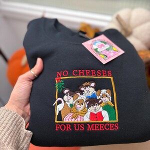 May include: Black sweatshirt with an embroidered design featuring a group of mice and the text "NO CHEESES FOR US MEECEES" in red. The mice are wearing various outfits. A pink tag is attached to the sweatshirt.