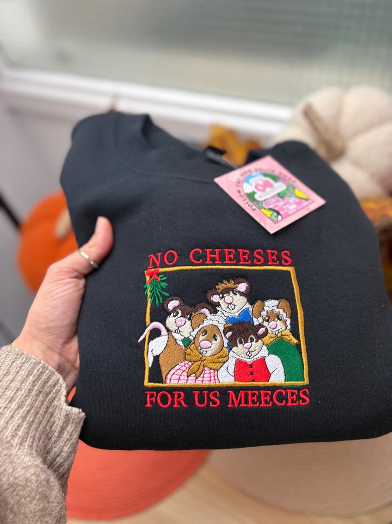 May include: Black sweatshirt with an embroidered design featuring a group of mice and the text "NO CHEESES FOR US MEECEES" in red. The mice are wearing various outfits. A pink tag is attached to the sweatshirt.