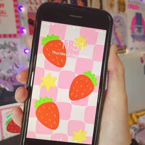 Könnte beinhalten: Ein rosa-weiß kariertes Handy-Hintergrundbild mit einem Erdbeer- und Sternendesign. Die Uhrzeit ist 11:51 Uhr und das Datum ist Donnerstag, der 5. September.