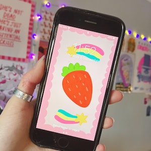 Könnte beinhalten: Ein rosa und weißer Telefonbildschirm mit einer Erdbeere und einem Regenbogen-Sternschnuppen. Die Uhrzeit ist 11:52 Uhr und das Datum ist Donnerstag, der 6. September. Der Text "Home drücken, um zu entsperren" befindet sich am unteren Bildschirmrand.