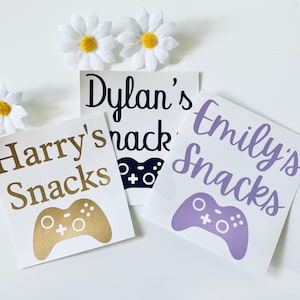 May include: Three white labels with black text and a game controller graphic. The labels read "Harry's Snacks", "Dylan's Snacks", and "Emily's Snacks".