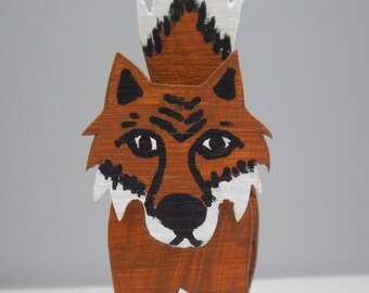 May include: A wooden fox figurine painted in brown, white, and black. The fox has a white tail with black markings and a black nose.