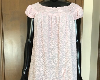 Puede incluir: Un camisón de encaje rosa con un dobladillo festoneado y bordados florales. El camisón tiene mangas cortas y un escote redondo.