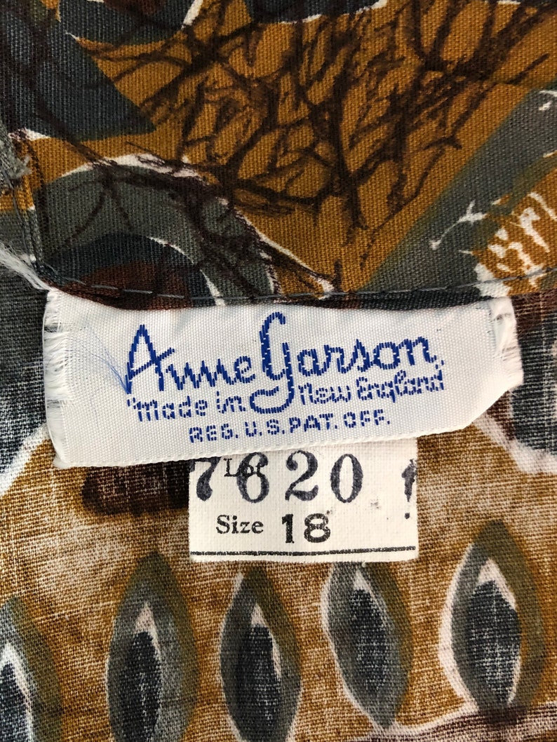 May include: Close-up of a vintage fabric with a repeating pattern in shades of brown, green, and white. The label reads "Anne Garson, Made in New England, Size 18".