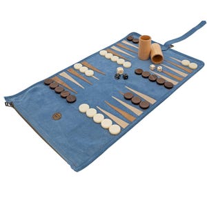 May include: A blue backgammon set with wooden game pieces and dice. The game board is rolled out on a blue surface, with brown and white triangles. Two wooden dice cups are also included.