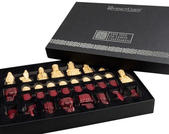 Puede incluir: Un juego de ajedrez de la Isla de Lewis en una caja negra. Las piezas de ajedrez son de color marfil y rojo. La tapa de la caja tiene el texto "The Regency Chess Company" y "The Isle of Lewis Chessmen". Las piezas están dispuestas en una bandeja forrada de terciopelo negro.
