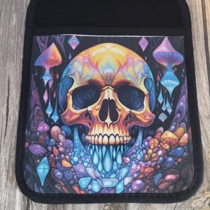 May include: A black pot holder featuring a colourful skull design. The skull is surrounded by a swirling pattern of blue, purple and orange. The skull has a blue and purple dripping effect.
