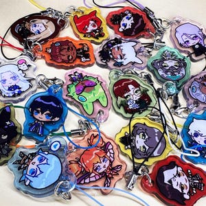 Puede incluir: Una colección de dijes de acrílico variados con coloridas ilustraciones de personajes estilo anime. Cada dije tiene una forma irregular única, un acabado brillante y está sujeto a un cordón fino y flexible para colgar como accesorio.