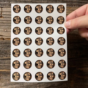 May include: A sheet of 36 round stickers with a black and gold design. The stickers say "Needs More Dirt" in a gold font.