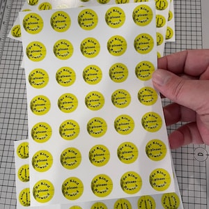 May include: A sheet of white paper with multiple yellow round stickers. Each sticker has the text "Be Kind please Rewind" in black text.