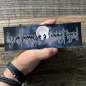 May include: A black and white sticker with a full moon and the text "Lycanthropy is a feminist issue!" in a gothic font.