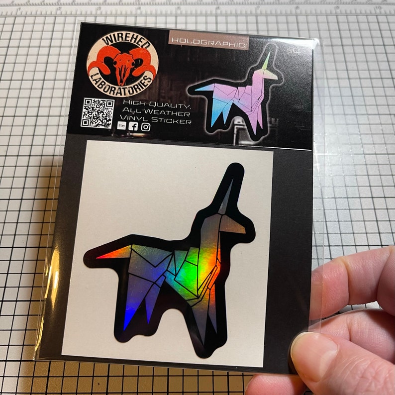 May include: A holographic sticker of a origami unicorn in a rainbow color scheme. The sticker is on a white background with a black border. The sticker is from Wired Laboratories.