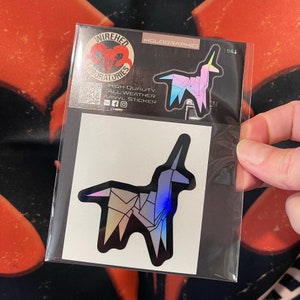 May include: A holographic sticker of a unicorn with a rainbow iridescent finish. The sticker is on a white background and has the text "WIREDHED LABORATORIES" and "HOLOGRAPHIC" printed on it.