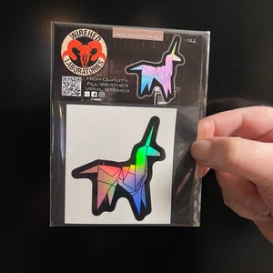 May include: A holographic sticker of a rainbow origami unicorn. The sticker is packaged in a clear plastic bag with a white backing card. The sticker is from Wiredhed Laboratories and says "High Quality, All Weather Vinyl Sticker".