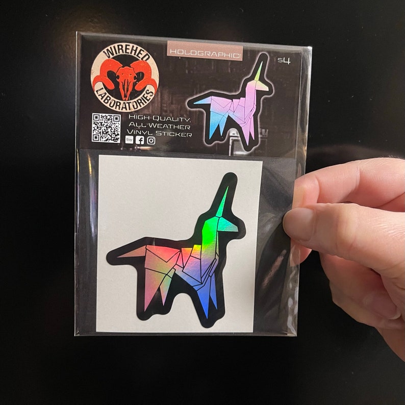 May include: A holographic sticker of a rainbow origami unicorn. The sticker is packaged in a clear plastic bag with a white backing card. The sticker is from Wiredhed Laboratories and says "High Quality, All Weather Vinyl Sticker".