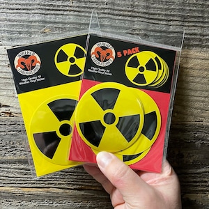 May include: A pack of five yellow and black radiation symbol stickers. The stickers are weatherproof and come in a sealed plastic bag. The packaging says "Wiredhed Laboratories" and "High Quality All Weather Vinyl Sticker".