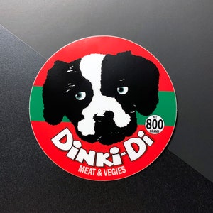 May include: A red, green, and white circular sticker with a black and white dog illustration. The sticker says "Dinki-Di Meat & Veggies" and "Net 800 Grams".
