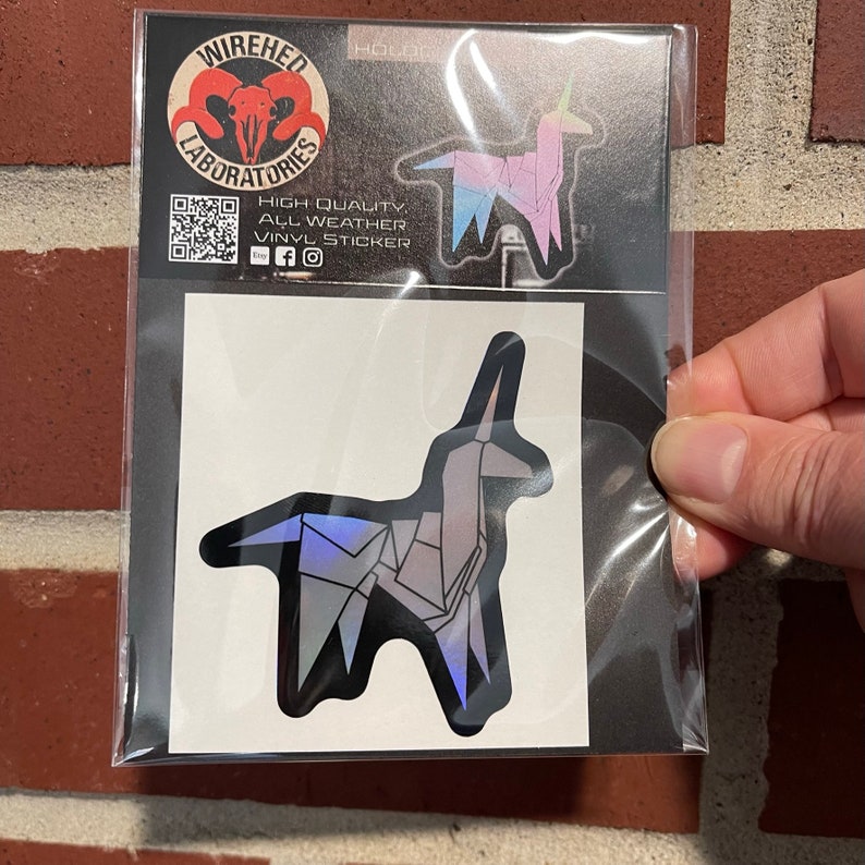 May include: A silver iridescent sticker of a unicorn origami design. The sticker is on a white background with a black border. The sticker is packaged in a clear plastic bag.