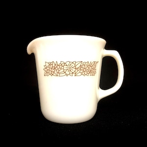 May include: A white ceramic mug with a black handle and the text "But First, Coffee" in a bold, black font. The mug is set against a blurred background, suggesting a cozy setting.