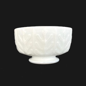 May include: A white milk glass bowl with a raised leaf design. The bowl has a pedestal base.
