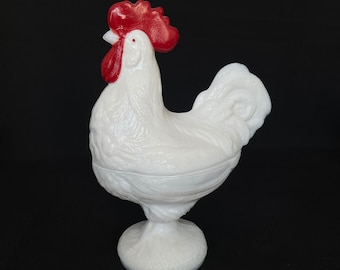 May include: White milk glass rooster with a red comb and wattles. The rooster is standing on a pedestal base.
