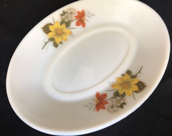 May include: White oval ceramic saucer with a floral design. The design features yellow, orange, and white flowers with green leaves.