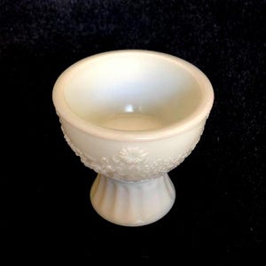 Op de afbeelding: Een witte melkglas voetkom met een bloemenmotief. De kom is perfect om snacks of desserts te serveren.
