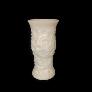 Könnte beinhalten: Eine weiße Milchglasvase mit einem erhabenen Blumendesign. Die Vase ist etwa 15 cm hoch.