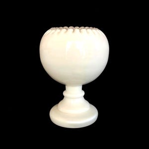 May include: A white ceramic pedestal bowl with a scalloped rim. The bowl is round and has a smooth, glossy finish.