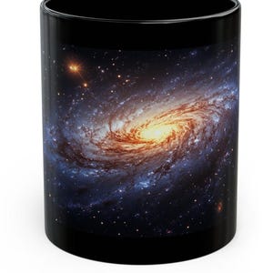 May include: Black coffee mug with a colorful spiral galaxy image printed on it. The galaxy is a swirling mix of blue, orange, and yellow with a dark background of stars.