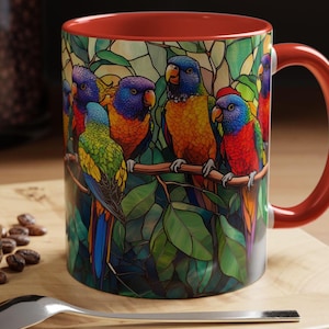 May include: A red and white ceramic mug with a colorful stained glass design of parrots in a leafy jungle setting.