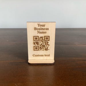 May include: A wooden sign with a QR code and the text "Your Business Name" and "Custom text".
