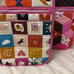 Peut inclure: Deux sacs fourre-tout roses avec des motifs patchwork matelassés. L'un présente une grille de carrés avec diverses illustrations, dont un lion et une fleur. L'autre a un motif géométrique avec des tissus roses et oranges.