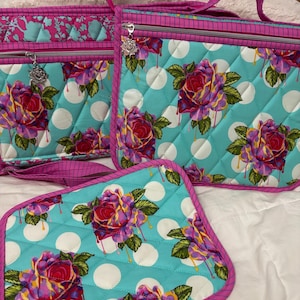 May include: A set of quilted bags and a pot holder. The turquoise fabric features large white polka dots and a floral pattern of red, purple, and yellow roses. The edges are trimmed in pink. The set includes a tote bag and a smaller bag.