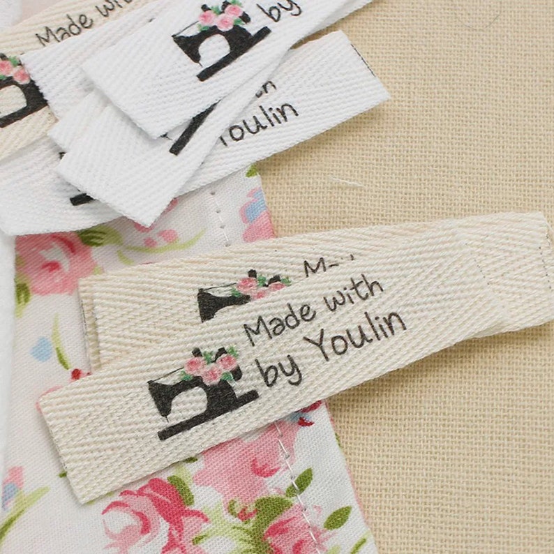 May include: A set of white and natural fabric labels with a sewing machine design and the text "Made with by Youlin".