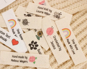 Puede incluir: Una colección de etiquetas de tela de algodón blanco con varios diseños y textos. Las etiquetas incluyen un arcoíris, una huella de pata, un girasol, un corazón, una rosa, una mariposa, una bola de hilo y agujas de tejer, y el texto "Hand Knit by Laurie Miller", "Crocheted by Jessica", "Shop Name Made With Love", "Shop Name Made With Love", "Custom Text Handmade", "Hand made by Melissa Weyers", y "Busy".