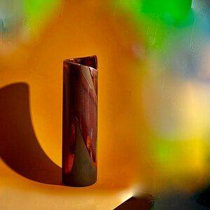 以下が含まれることがあります： ねじれたテクスチャのあるデザインの濃い茶色のセラミック花瓶。花瓶は黄色の表面の上に置かれています。