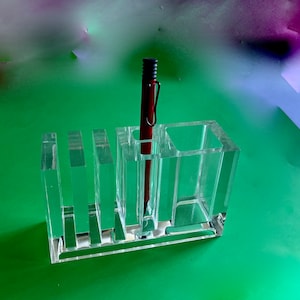 May include: A clear acrylic desktop organizer with five compartments. A red pen is in the center compartment.