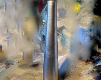 May include: A tall, silver-colored vase with a conical base and cylindrical body. The vase has a smooth, metallic finish and stands upright. The background features a colorful, abstract design with various hues and textures.