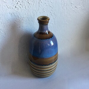 Puede incluir: Un jarrón de cerámica azul y marrón con un diseño a rayas. El jarrón tiene un cuerpo redondeado y un cuello estrecho.