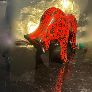 Può includere: Statuetta decorativa di toro nero e rosso. Il toro è dipinto con una finitura lucida e presenta intricati motivi rossi su una base nera. La statuetta ha la testa rivolta verso il basso ed è in piedi su quattro zampe.