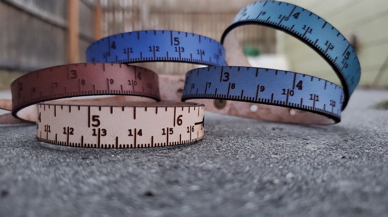 May include: Four leather bracelets with ruler markings. The bracelets are in shades of blue and brown. The markings on the bracelets are in inches.